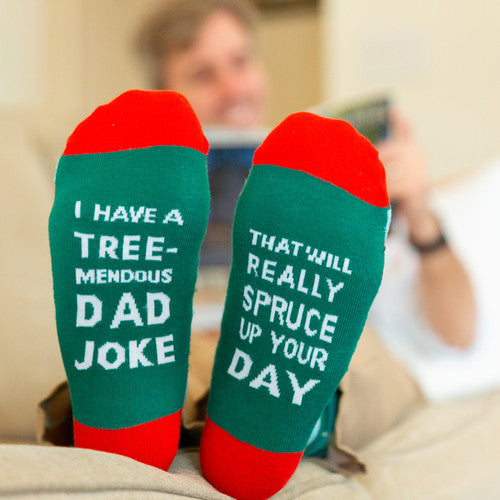Green socks with red accents worn by a person, featuring humorous text that reads I have a tree-mendous dad joke that will really spruce up your day
