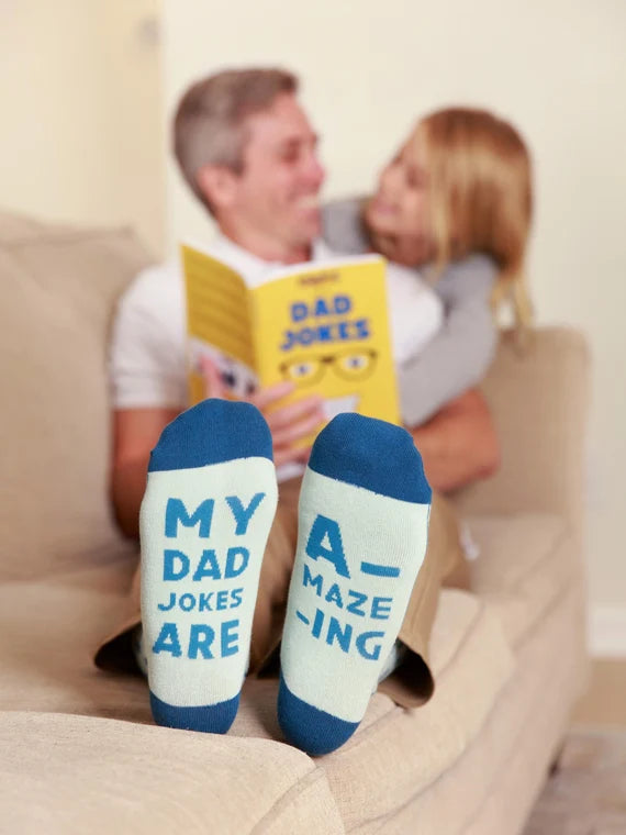 A Dad siting with a daughter while they hug and read Dad Joke Book while Dad is wearing My Dad Jokes Are Amazing Funny Socks for Men by FunnyFeet