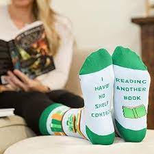 Person wearing socks for readers with humorous text, sitting on a couch reading a book.