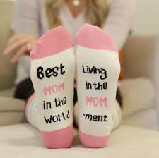 Pair of socks with text 'Best Mom in the World' and 'Living in the Mom Moment' on a mom sitting in a chair with her feet up on a stool